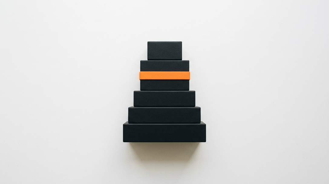 Stack of five matte black blocks on white with one orange band