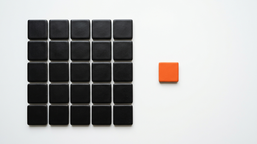 Grid of matte black square tiles on white with one orange tile apart