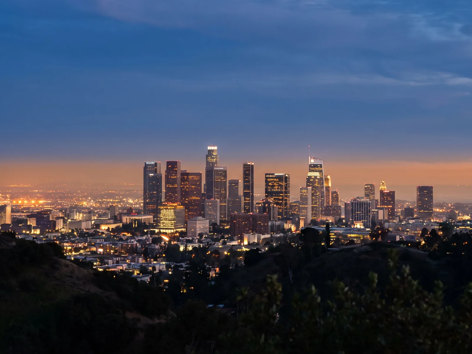 The downtown Los Angeles skyline at dusk, seen from the hills with the city grid behind it