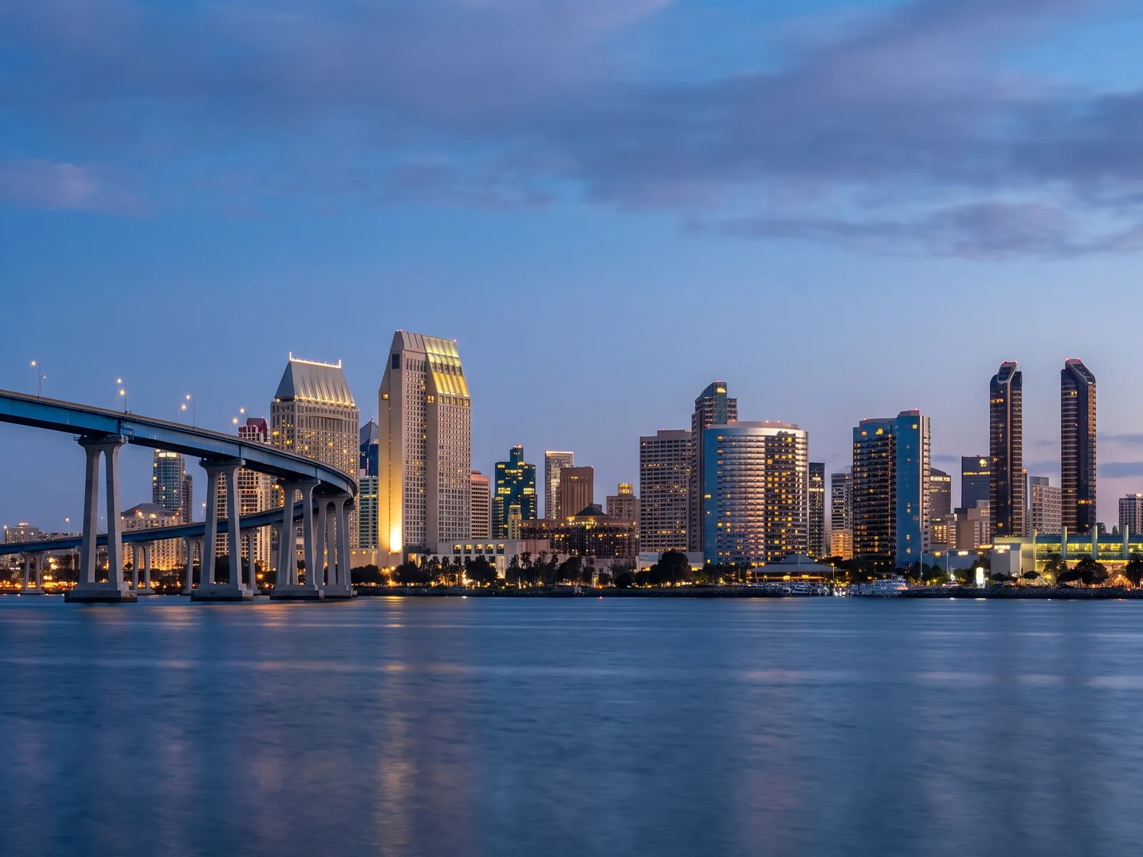 The downtown San Diego skyline at dusk, seen across the bay with the Coronado bridge at left