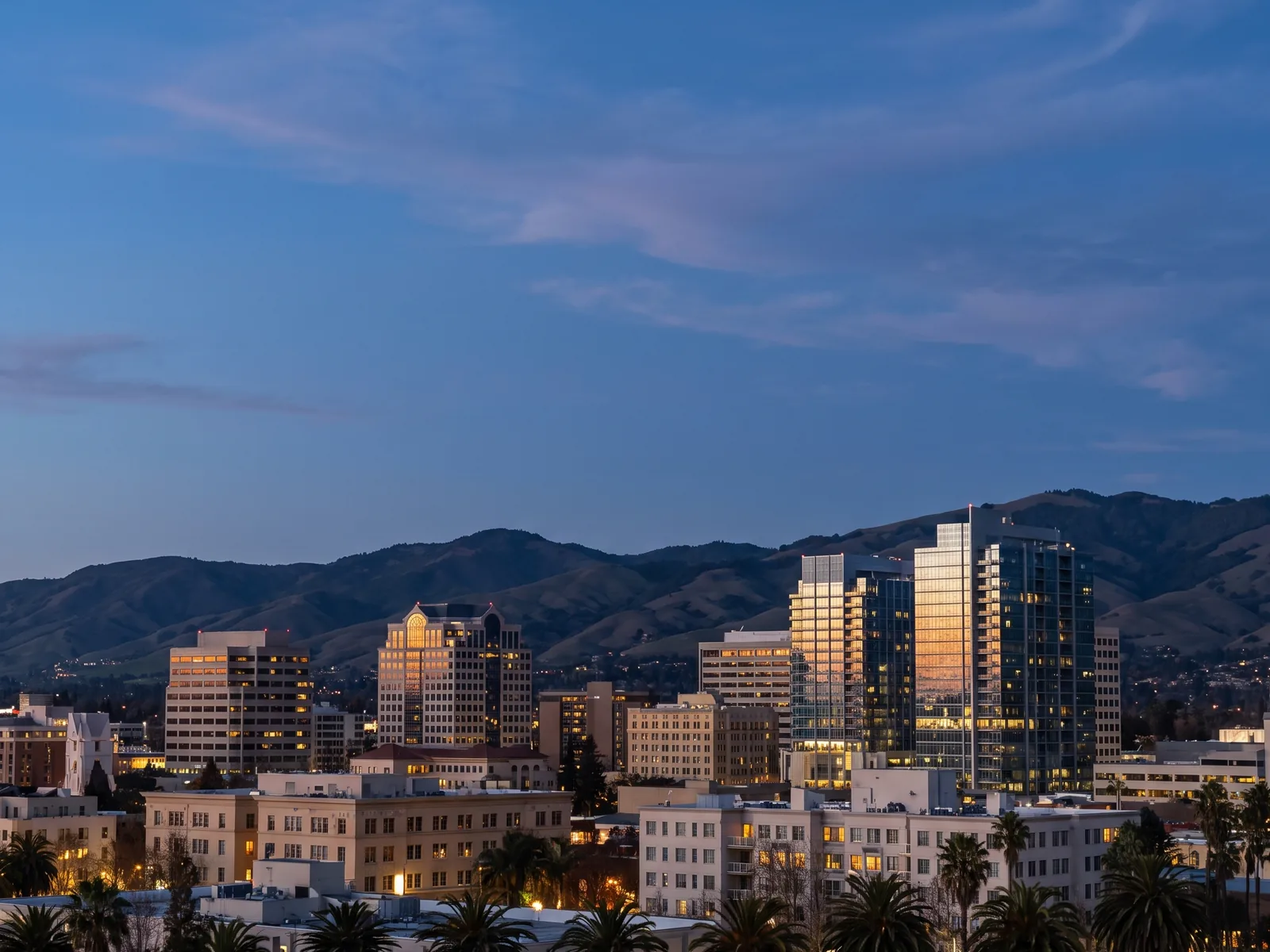 The downtown San Jose skyline at dusk against the Diablo Range, palms in the near ground